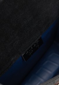 Interno di una borsa in suede nero con rivestimento blu liscio, caratterizzata da una piccola etichetta nera con testo bianco. La forma concava ne esalta la profondità.