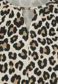 Leopardenmuster-Oberteil mit V-Ausschnitt, hellbeigem Grundton mit schwarzen und braunen Flecken, strukturiertem Stoff und sichtbaren Nähten.