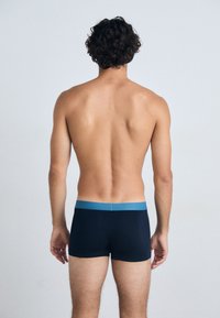 Boxer shorts bleu marine avec une ceinture bleu clair, design sans couture et texture douce, montrés de dos sur un torse nu.
