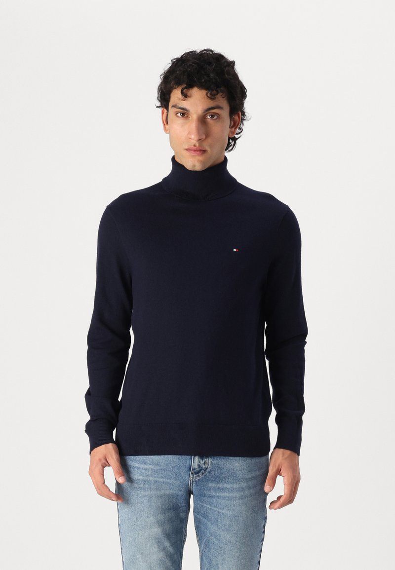 Navyblauer Rollkragenpullover aus weichem Material, mit langen Ärmeln, körpernahem Schnitt und einem kleinen Logodetail auf der Brust.