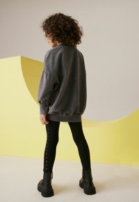 Grå oversized sweatshirt med ribbade muddar, kombinerad med svarta leggings som har metalliska nitar längs sidorna, och klumpiga svarta stövlar.