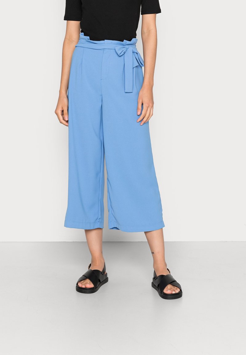 Blå vida byxor i mjukt tyg, med hög midja och bälte som knyts. Klas i svart platta sandaler.