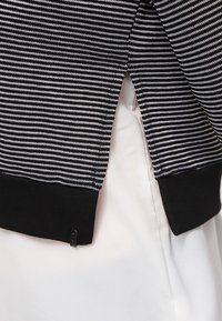 Pull à rayures noires et blanches avec un tissu texturé, un ourlet côtelé noir uni et des fentes latérales.