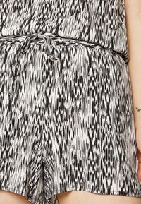 Macacão em preto e branco com padrão e cintura com cordão. Apresenta um tecido texturizado e fluido com um design abstrato em ziguezague por toda a peça.