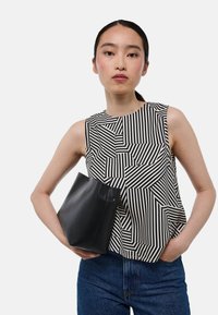 Haut sans manches à motif géométrique noir et blanc en tissu, associé à une pochette en cuir noir et un pantalon en denim bleu.