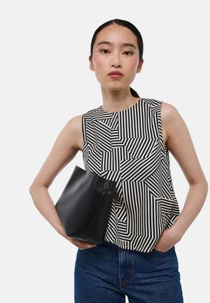 Haut sans manches à motif géométrique noir et blanc en tissu, associé à une pochette en cuir noir et un pantalon en denim bleu.
