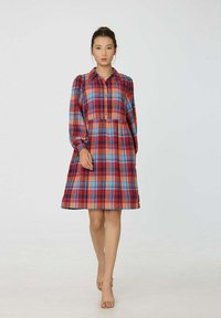 Robe à carreaux rouge et bleu, manches longues, devant boutonné, silhouette évasée, texture du tissu semble douce, longueur genoux, assortie à des sandales beiges.