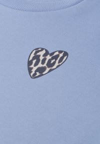 Tissu bleu clair avec une petite pièce en forme de cœur présentant un imprimé léopard noir et blanc près du col.