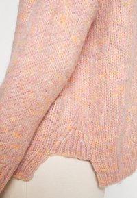 Stickad tröja i mjuk pastellrosa med gula inslag. Har en avslappnad passform, ribbad nederkant och strukturerad sömnad.