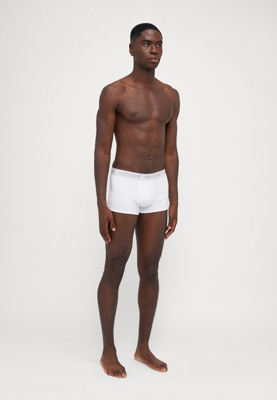 Boxers de algodón blanco con una cinturilla elástica gris que presenta el logo "Roberto Cavalli", el modelo está descalzo contra un fondo claro.