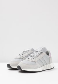 Scarpe da ginnastica grigie con parte superiore in suede e mesh, dotate di tre strisce bianche, collare imbottito e suola in gomma texturizzata.