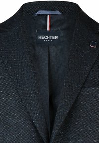 Dunkel strukturierte Blazer-Innenseite mit einem dezenten Muster, Etikett mit der Aufschrift "HECHTER PARIS" und einem rot-weiß-blauen Akzentstreifen.