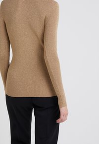 Beige ribbad tröja med lång ärm, detaljer i guldtråd, figursydd design, textil med struktur, matchad med svarta byxor.