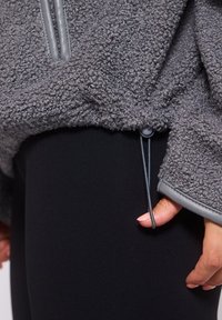 Pullover grigio in pile con tessuto testurizzato, caratterizzato da una coulisse all'orlo e bordi a contrasto. Abbinato a leggins neri.