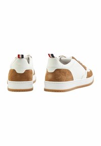 Sneaker aus weißem Kunstleder mit braunen Wildlederpaneelen, runder Spitze, flacher Gummisohle und einem kleinen roten, weißen und marineblauen Akzent an der Ferse.