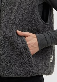 Gray fleece vest with textured fabric, open sides, and a visible pocket. Features a small "SENSES" label at the bottom.