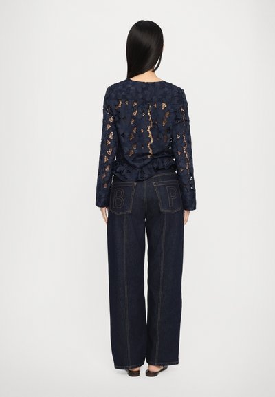 Navy lace top with floral patterns, ruffled hem, paired with high-waisted dark denim jeans featuring contrasting "B P" embroidery on pockets.