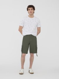 T-shirt bianca con piccoli motivi di barche a vela blu marina, abbinata a pantaloni cargo verdi oliva di lunghezza al ginocchio con tasche laterali. Calzature casual.