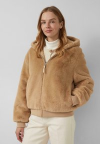 Fuzzy beige hoodie gemaakt van zachte stof, met een frontale rits, geribde manchetten en zijzakken. Draagt over een lichte turtleneck.