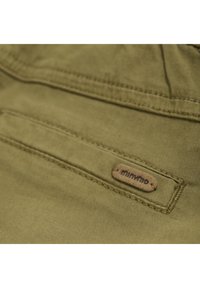 Khaki stof met een gladde textuur, voorzien van een gestikte zak en een tan leren etiket met de opdruk "minymo."