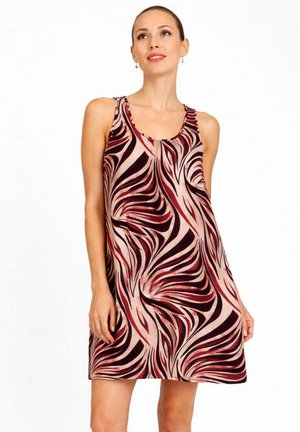 Donna che indossa un vestito senza maniche al ginocchio con un motivo astratto vorticoso rosso, nero e beige, in piedi su sfondo bianco.