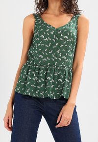 Blusa floral verde con cuello en V, diseño sin mangas, frente con botones y cintura con peplum. Confeccionada en tela ligera y texturizada.