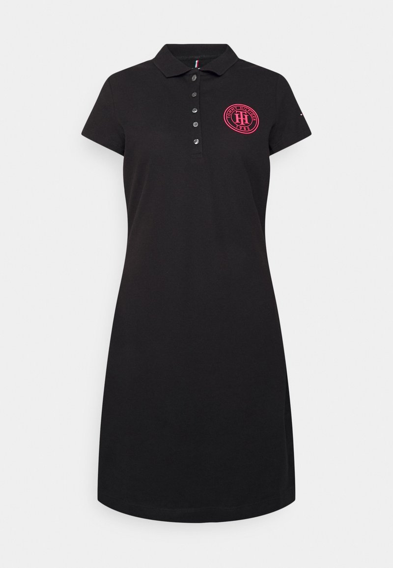 Robe polo noire en coton, dotée d'un col, d'une patte de boutonnage et d'un logo circulaire rose bien visible sur la poitrine. Manches courtes, coupe décontractée.