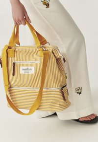Bolso tote a rayas amarillas con asas dobles, bolsillos con cremallera y acentos de cuero marrón. Hecho de una tela resistente con una forma estructurada.