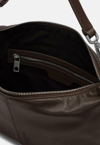 Brązowa skórzana torba z zamkiem błyskawicznym, z czarną podszewką wewnętrzną, srebrnymi okuciami i wszytą etykietą.