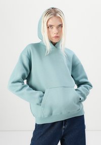 Lichtblauwe hoodie gemaakt van zachte stof, met een kangoeroezak, ribgebreide boorden en een minimalistisch logo-detail.