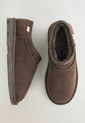Braune Wildleder-Ankelstiefel mit einem weichen, plüschigen Futter, runder Zehenpartie und Gummisohle. Mit kontrastierenden Nähten und einem kleinen Markenetikett.