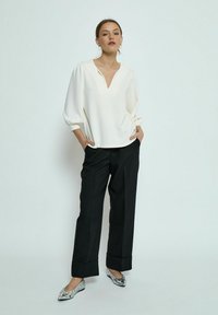 Witte blouse met lange mouwen en V-hals, gecombineerd met zwarte, wijde broek. Heeft een relaxte pasvorm en een gladde textuur. Geaccentueerd met platte schoenen.