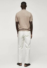 Polo shirt marron à manches courtes, pantalon blanc droit et sandales noires. Le tissu semble lisse avec une coupe décontractée.