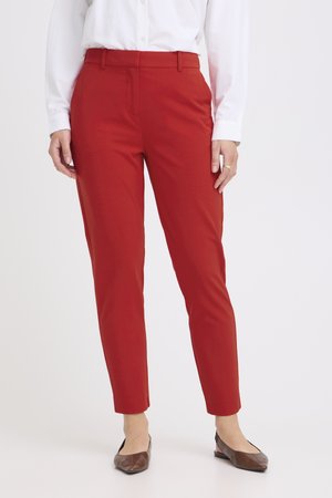 Femeie purtând pantaloni roșii, mulat, lungime până la gleznă, asortați cu o cămașă albă cu mâneci lungi și pantofi maro cu talpă joasă.