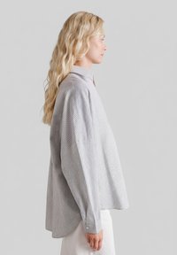 Koszula z długim rękawem w kratę, z kołnierzem stójką, luźnym krojem i miękką tkaniną w odcieniach szarości i bieli.