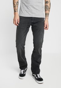 Svarta denimjeans med rak passform, med en klassisk femficksdesign, bärs med en grå t-shirt och svarta sneakers.