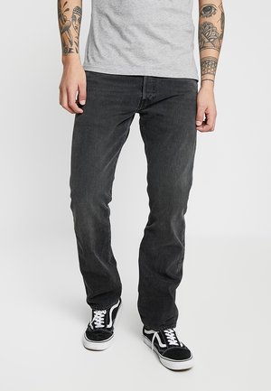Jeans de mezclilla negra de corte recto, con un diseño clásico de cinco bolsillos, combinados con una camiseta gris y unas zapatillas negras.