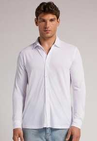 Camisa blanca de manga larga, tela suave, diseño con cuello, con botones al frente, forma ajustada, ligero brillo, combinada con jeans azul claro.