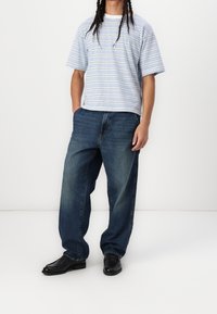 Camiseta de manga corta a rayas en azul claro y blanco, combinada con unos vaqueros de Pierna Ancha azules. Unos zapatos de cuero negros completan el conjunto.