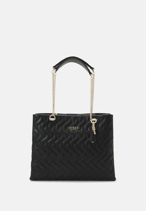 Bolso de mano acolchado negro con una forma estructurada, detalles en cadena plateada y un asa en la parte superior. Presenta un logo y un pequeño charm decorativo.