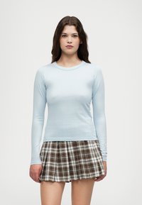 Light blue long-sleeve top paired with a plaid pleated skirt in brown, white, and beige colors. Smooth texture with a fitted design.