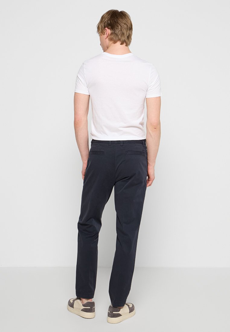 Dunkelblaue Hosen mit geradem Bein, aus Baumwolle. Mit Gürtelschlaufen, zwei Gesäßtaschen und einer lässigen Passform. Getragen mit einem weißen T-Shirt.