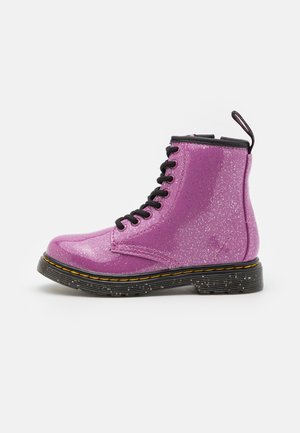 Botines de tobillo rosa brillantes con cordones negros, suela de goma y costuras amarillas. Cuenta con una lengüeta en el talón para facilitar su uso.