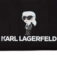 Black fabric bag featuring a cartoon figure in sunglasses and white text reading "KARL LAGERFELD." The design has minimalistic accents.