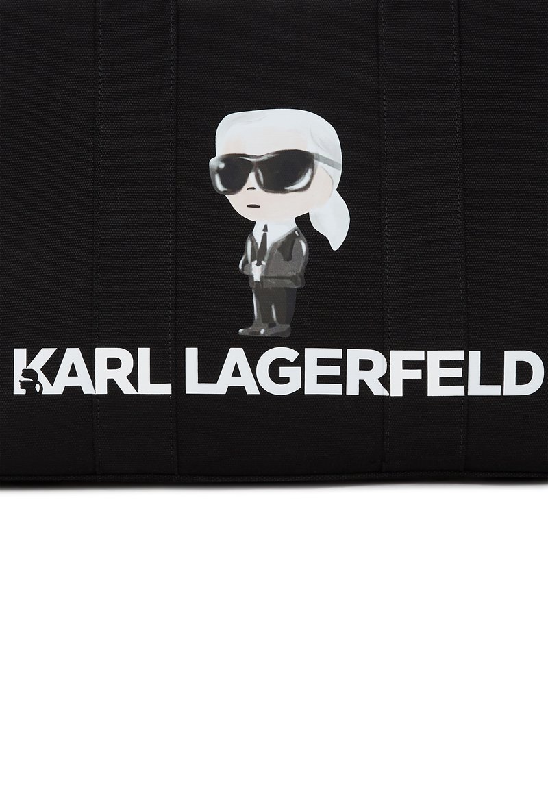 Sac en tissu noir avec une figure de dessin animé portant des lunettes de soleil et un texte blanc indiquant "KARL LAGERFELD". Le design présente des accents minimalistes.