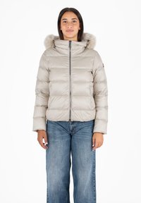 Puffy beige jas met een bontomzoomde capuchon, een rits aan de voorkant en gestikte panelen. Gecombineerd met lichtblauwe wijde jeans.
