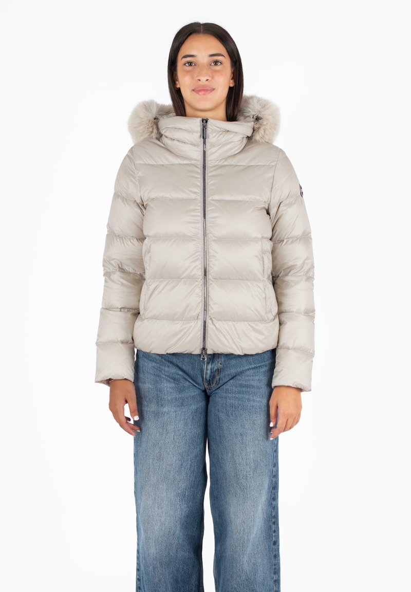 Puffy beige jas met een bontomzoomde capuchon, een rits aan de voorkant en gestikte panelen. Gecombineerd met lichtblauwe wijde jeans.
