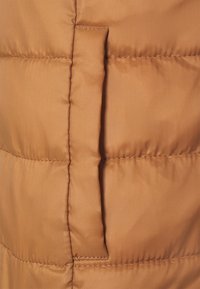 Veste matelassée sans manches de couleur marron clair en tissu synthétique lisse, présentant un motif matelassé horizontal et une poche latérale avec rabat cousu.