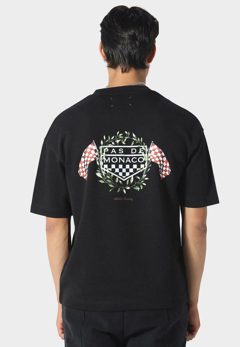 Sort bomulds t-shirt med et grafisk design på ryggen, der inkluderer ternede flag, en krans og teksten "PAS DE MONACO." Korte ærmer.