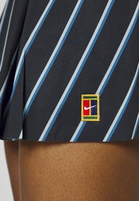 Falda negra con rayas verticales en azul y azul claro. Presenta un parche cuadrado con el logo de Nike en rojo, amarillo y verde en el dobladillo.